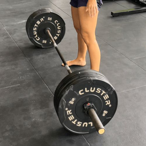 A barbell on a gym floor, bare feet beside it