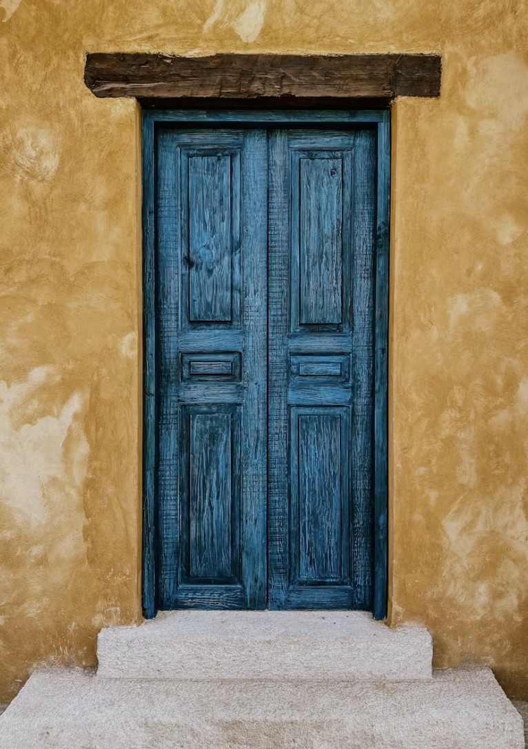A weathered blue double door in a stone archway, set into a warm ochre wall